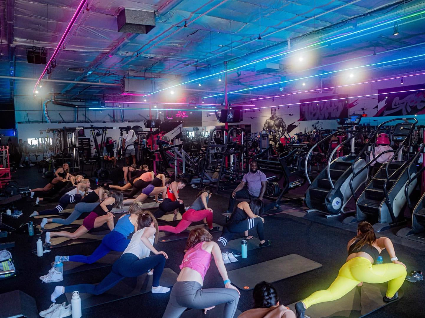 A group class training together under the neon lighting on the Fit Club gym floor